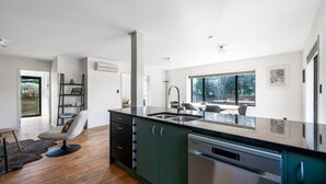 A modern kitchen with a large island, built-in appliances, and a view of the outdoors. - Wanaka close to town | Modern | Fireplace & Heatpumps | Sleeps 6 (Wānaka)