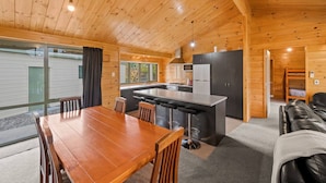 Una cabaña moderna de troncos con interior de madera, un comedor, una cocina y una sala de estar con sofá.