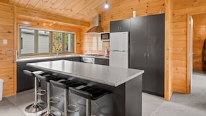 Una cocina moderna con una isla central, taburetes de bar, un lavamanos de acero inoxidable y un horno empotrado.