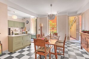 A spacious kitchen with a dining area, featuring a checkered floor, wooden furniture, and a view of the outdoors. - Grand Green Terrace Apartment, Menton, France (Menton)