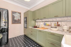 A kitchen with green cabinets, a marble countertop, and a black and white tiled floor. - Grand Green Terrace Apartment, Menton, France (Menton)