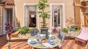 An outdoor dining area with a round table set for a meal, surrounded by chairs and potted plants.