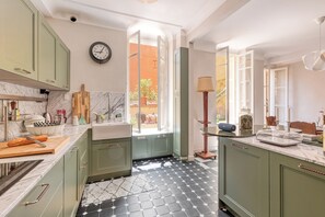 A kitchen with green cabinets, a marble countertop, a clock, and a view to the outside. - Grand Green Terrace Apartment, Menton, France (Menton)