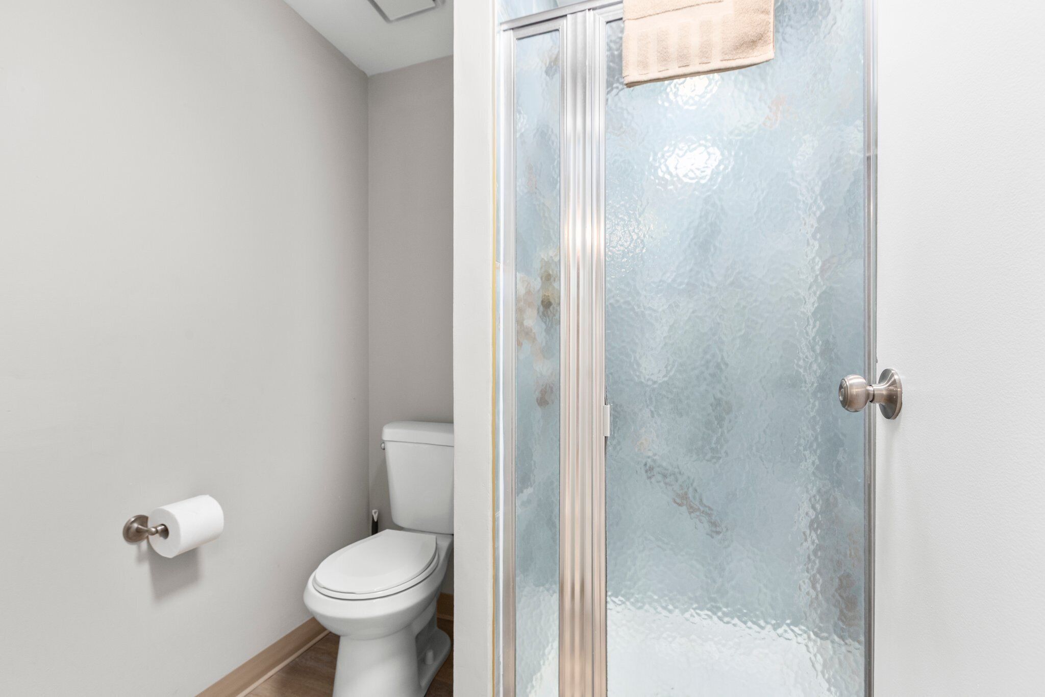 Un baño con inodoro, cabina de ducha de vidrio y una toalla colgada en la puerta.