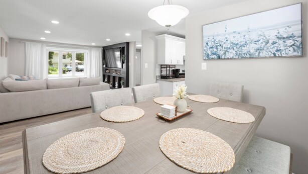 A modern dining area with a wooden table, woven placemats, and a vase with flowers.