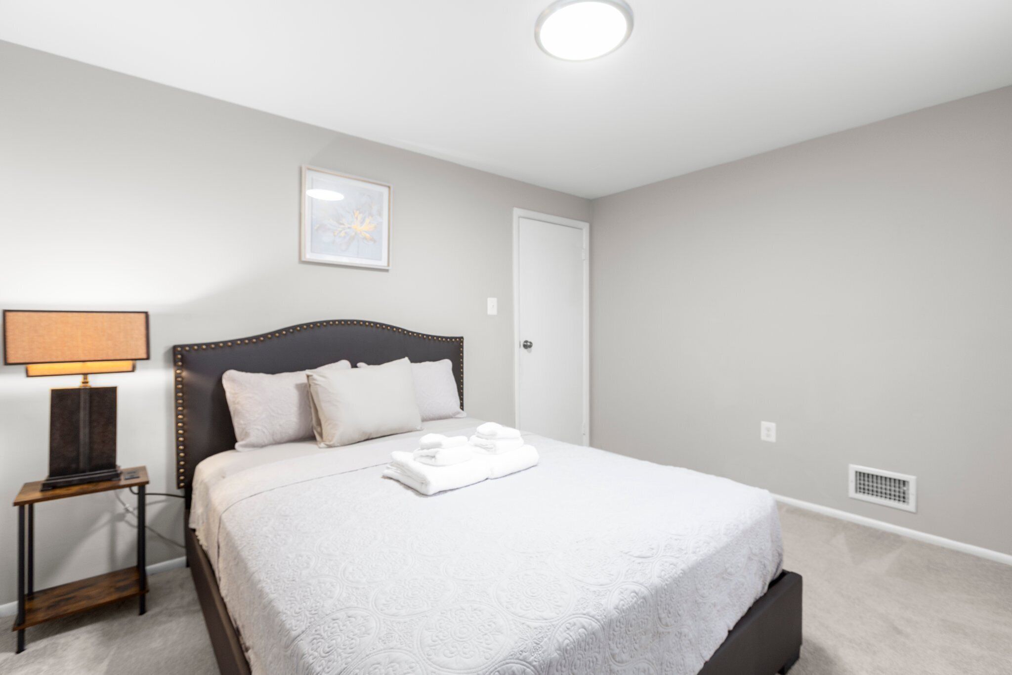 A bedroom with a bed, a nightstand, a lamp, and a framed picture on the wall.