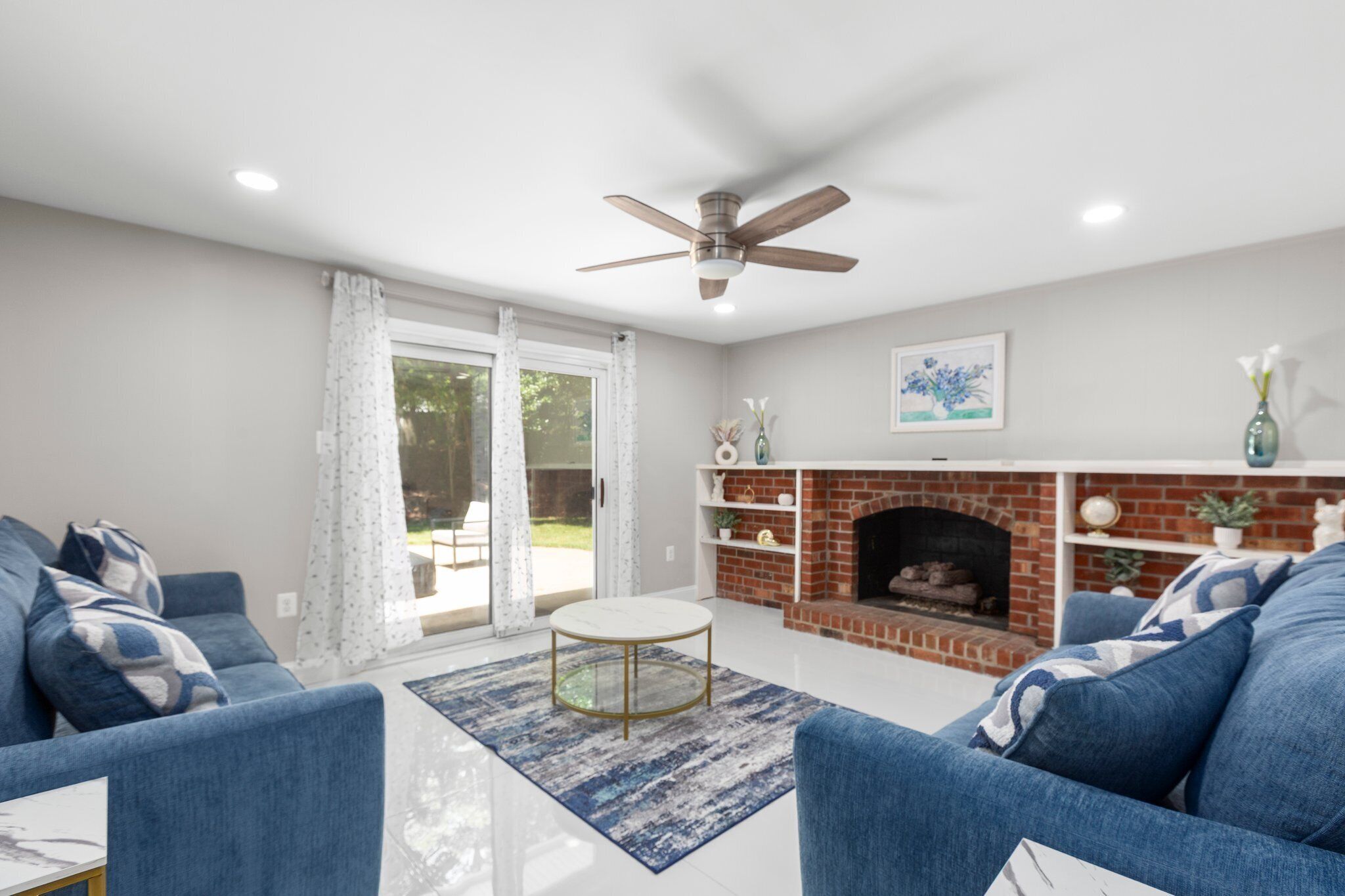 A living room with a fireplace, blue sofas, a coffee table, and a ceiling fan.