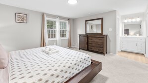 A bedroom with a bed, a dresser, a mirror, and a window with curtains.