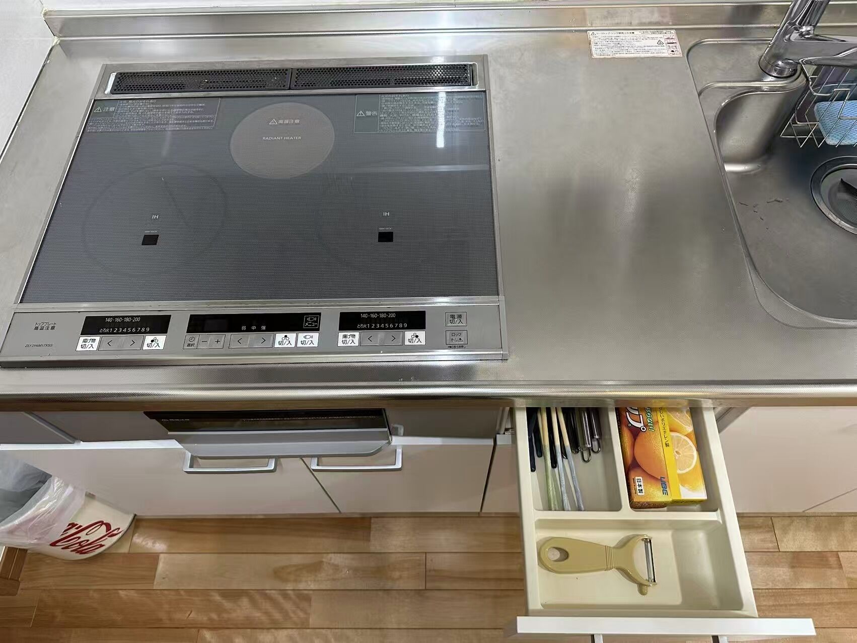 A kitchen with a stainless steel range hood, a sink, and a drawer with kitchen utensils.
