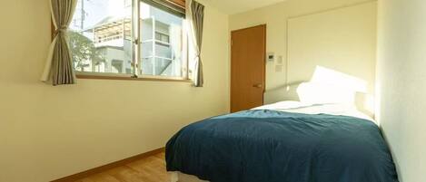 Une chambre à coucher avec un lit, une fenêtre avec des rideaux, un plancher en bois et une porte.