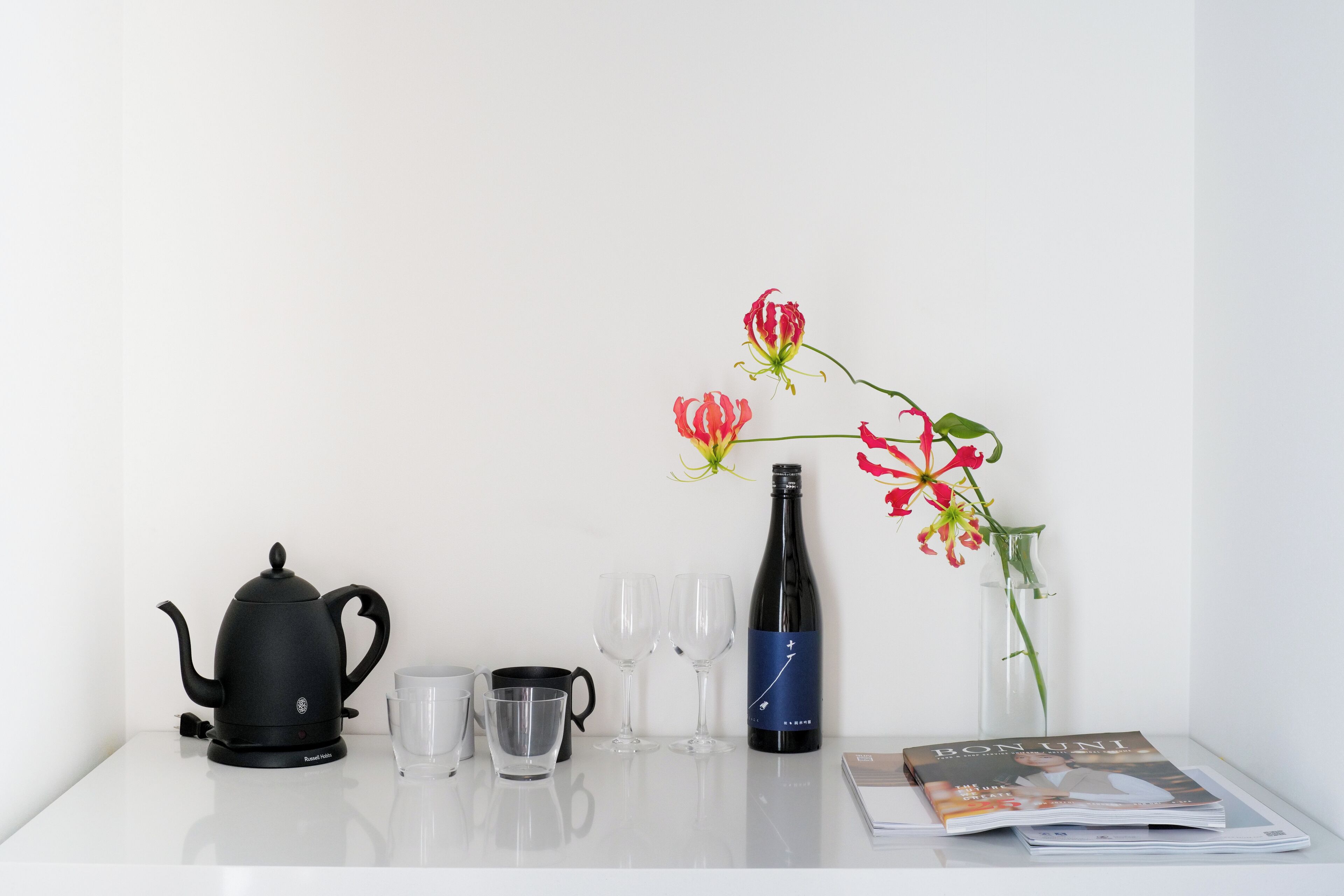 A table with a black teapot, two glasses, a wine bottle, and a magazine.