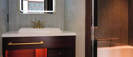 Un baño moderno con un espejo grande, un lavabo blanco, un mueble de tocador oscuro y una ducha con mampara de vidrio.