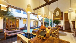 A spacious indoor area with a pool, wooden furniture, and hanging pendant lights.