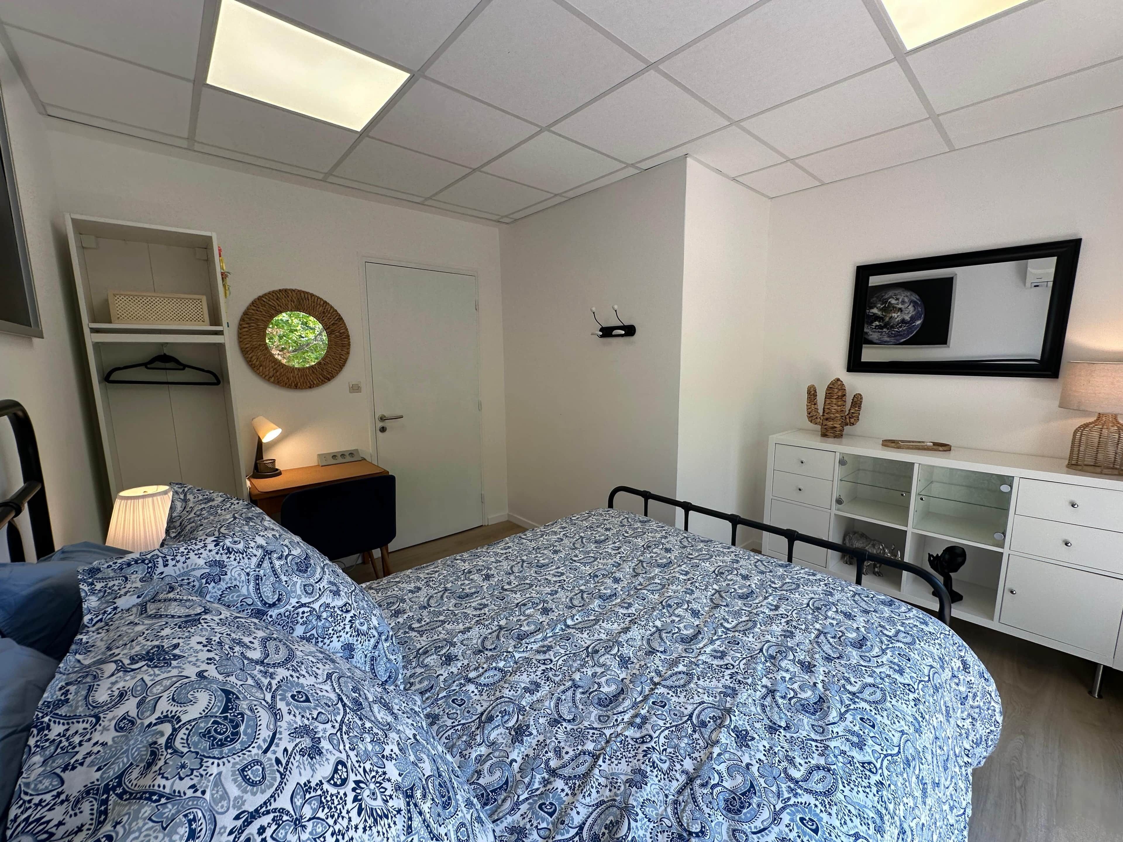 A bedroom with a bed, a desk, a chair, a wardrobe, and a mirror.