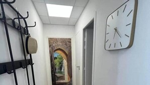 A hallway with a wooden floor, a black bench, a wall-mounted clock, and a stone archway leading to another room. - L'étape Aixoise - Terrace apartment car park Rotonde centre (Aix-en-Provence)