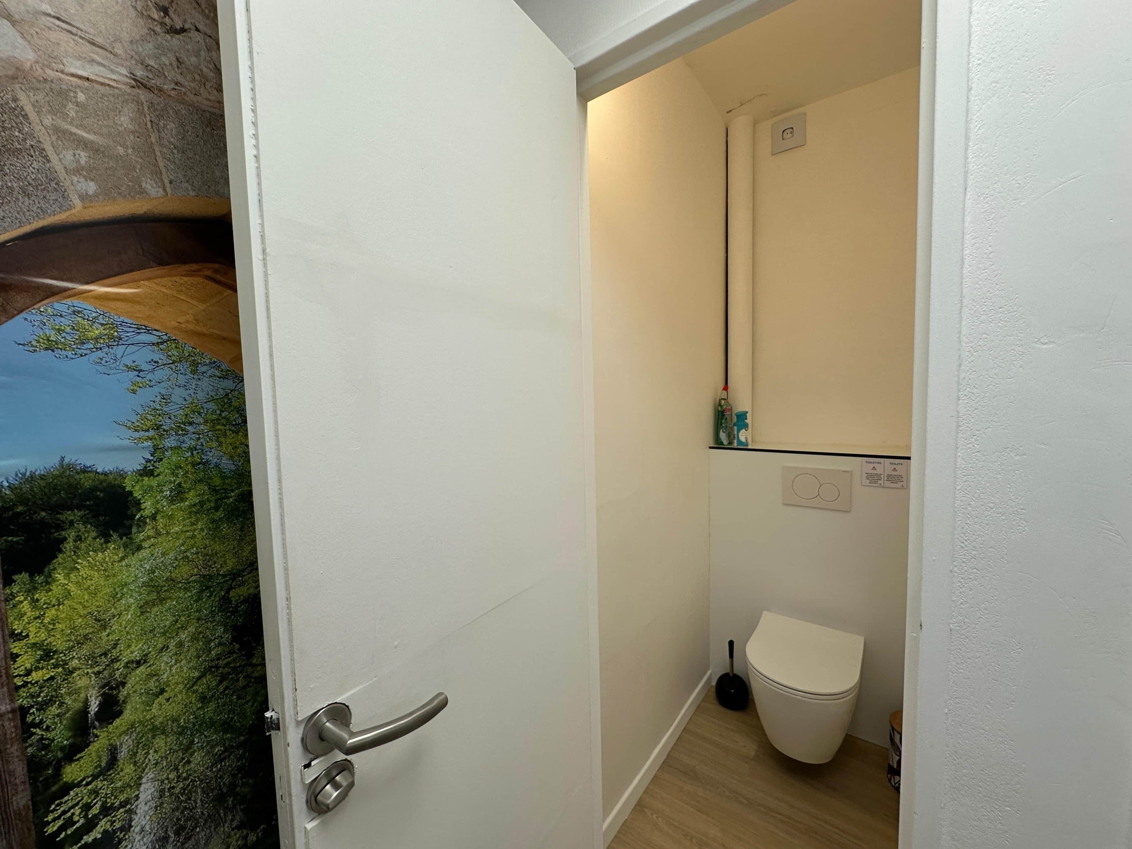 Une salle de bain équipée de toilettes, d’une ventouse et d’une petite étagère contenant des articles de toilette.