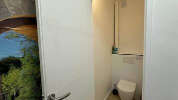 Une salle de bain équipée de toilettes, d’une ventouse et d’une petite étagère contenant des articles de toilette.
