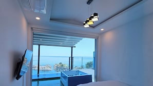 A modern bedroom with a large bed, a TV mounted on the wall, and a view of the sea through the sliding glass door. - Exit Full Villa (Yeongdeok)