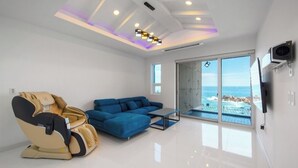 A modern living room with a massage chair, blue sofa, and a large window offering a view of the ocean. - Exit Full Villa (Yeongdeok)