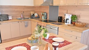 A modern kitchen with wooden cabinets, a built-in oven, a coffee maker, and a dining area with a table set for two.