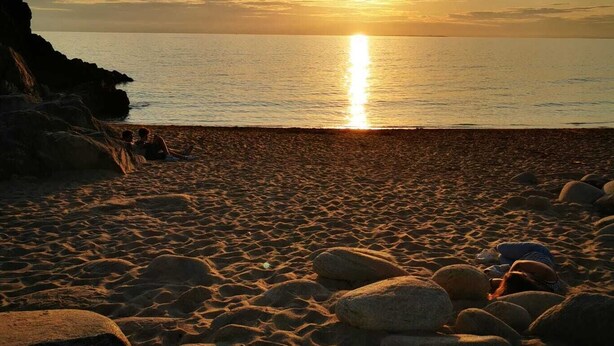 A beach with large rocks and the sun setting over the water.