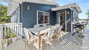 Eine überdachte Terrasse mit Essbereich, Grill und Topfpflanzen.