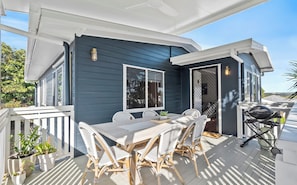 A covered outdoor patio with a dining table and chairs, a grill, and potted plants.