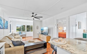 A spacious living room with a large TV, a ceiling fan, and a view of the outdoors.