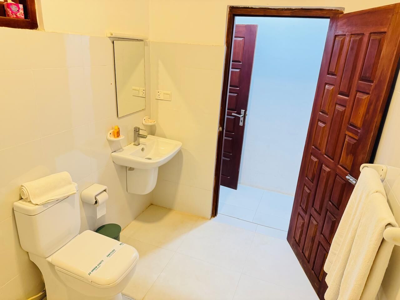A bathroom with a toilet, sink, and mirror. There is a wooden door leading to another room.