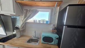 A compact kitchen with a sink, a microwave, a refrigerator, and a window with a view. - Coastal Caboose beach container home (Bolivar Peninsula)