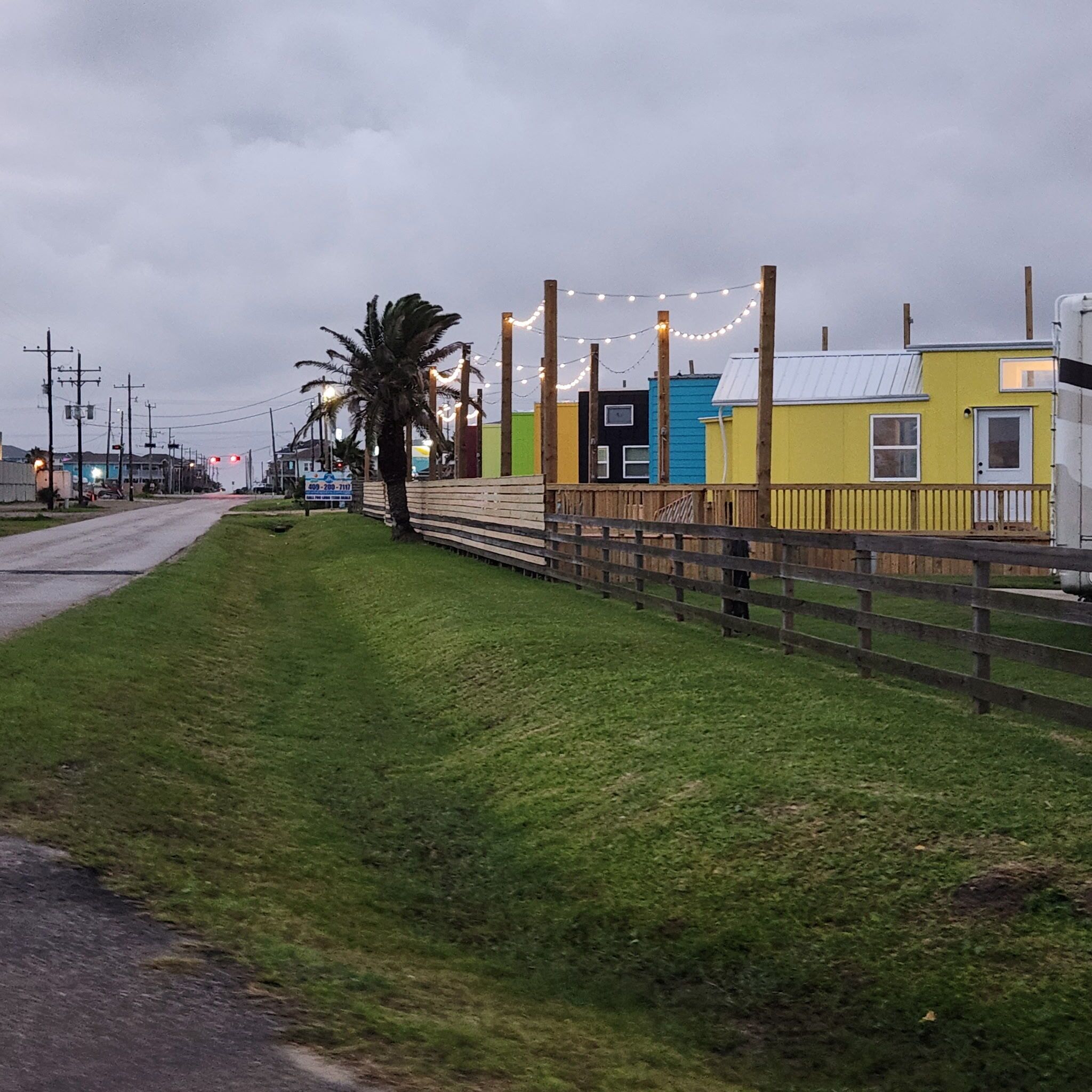 A roadside view with a grassy area, a wooden fence, and colorful buildings.