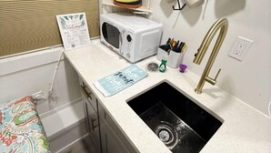 A compact kitchenette with a sink, microwave, and shelves.