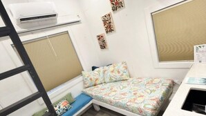 A compact room with a bed, a small desk, and a window with blinds.