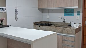 Una cocina moderna con muebles blancos, una estufa a gas y un lavamanos. Hay carteles que indican prohibido fumar y sin responsabilidad por daños.