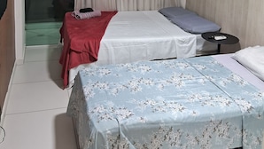 Habitación de hotel con dos camas, una mesita, ventilador de techo y ventana con cortinas.