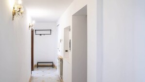 Ein schmaler Flur mit weißen Wänden, Holzboden und einer schwarzen Bank.