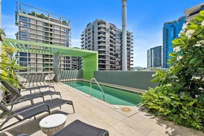 Piscina no terraço com espreguiçadeiras, cercada por vegetação e edifícios modernos.