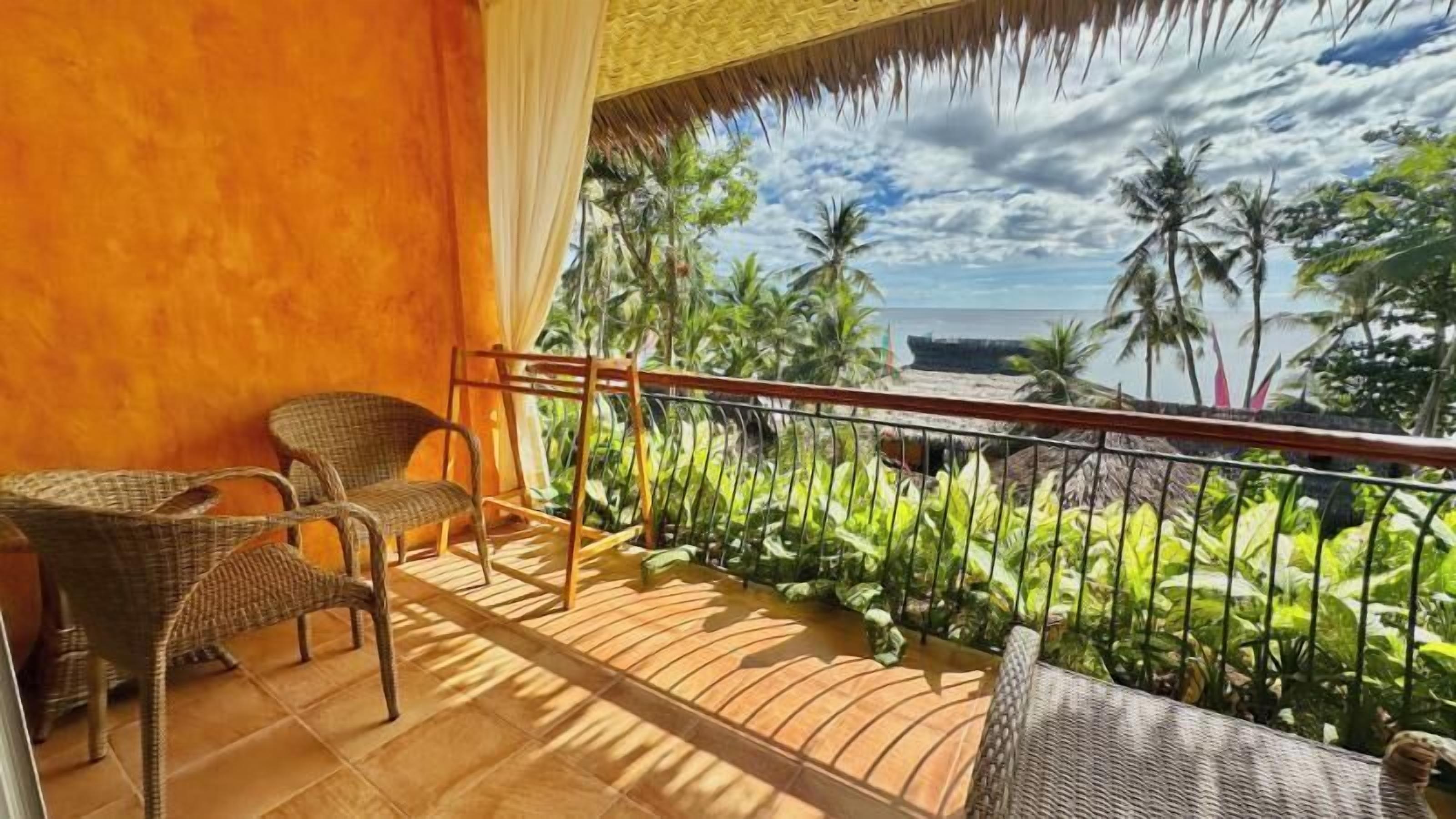 Un balcón con mobiliario de mimbre, vistas a palmeras y a la playa.