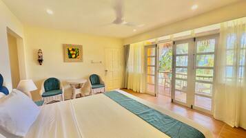 A hotel room with a bed, two chairs, a table, a ceiling fan, and a view of the outdoors through large sliding doors.