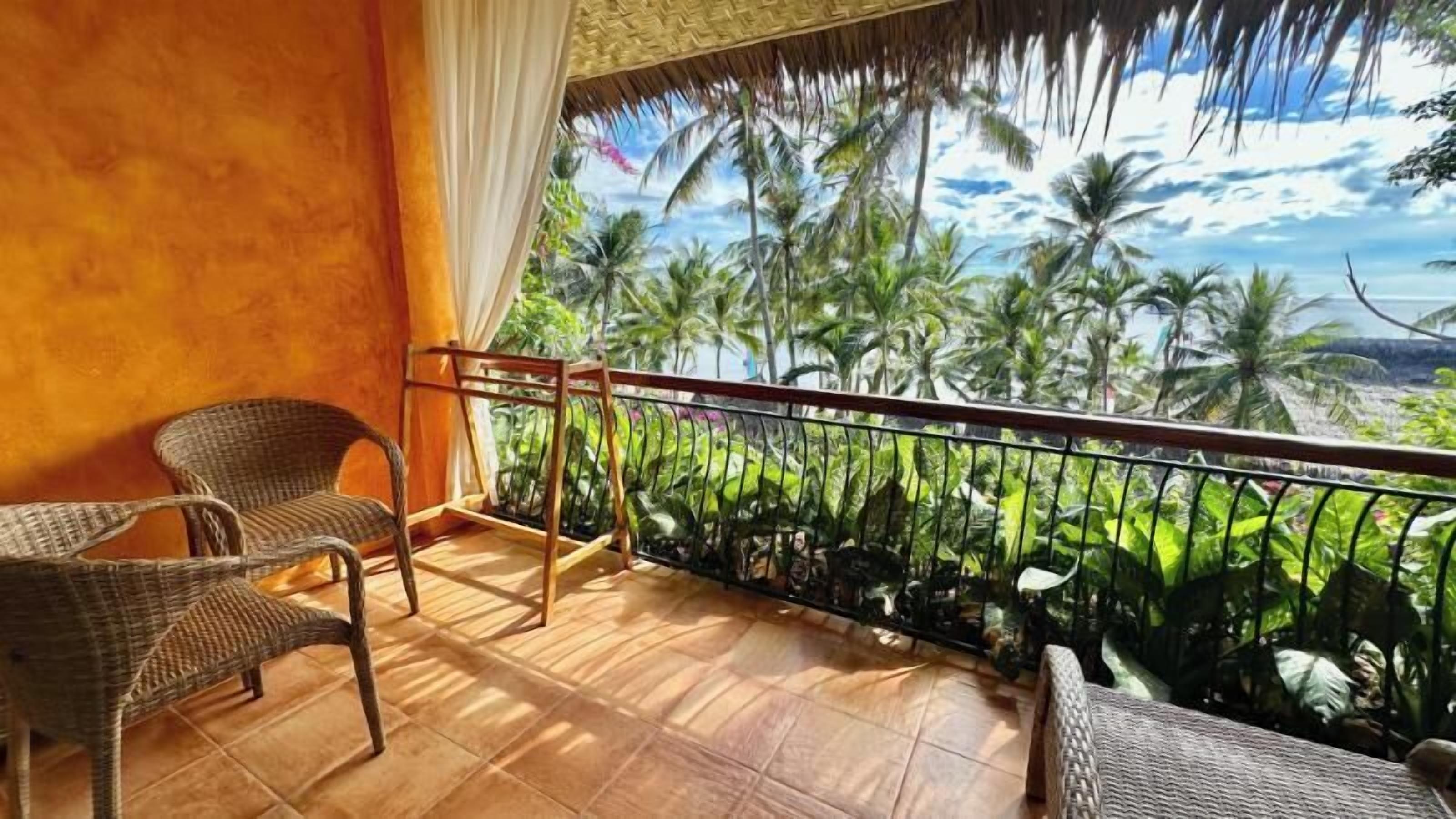 A balcony with wicker furniture, a view of palm trees, and a tropical landscape.