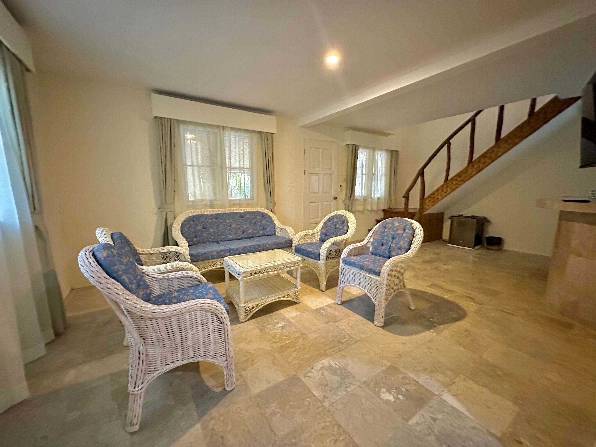 A spacious living area with a sofa, two armchairs, and a coffee table. A staircase is visible in the background.