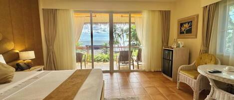A hotel room with a bed, a desk, a chair, a table, and a view of the ocean.