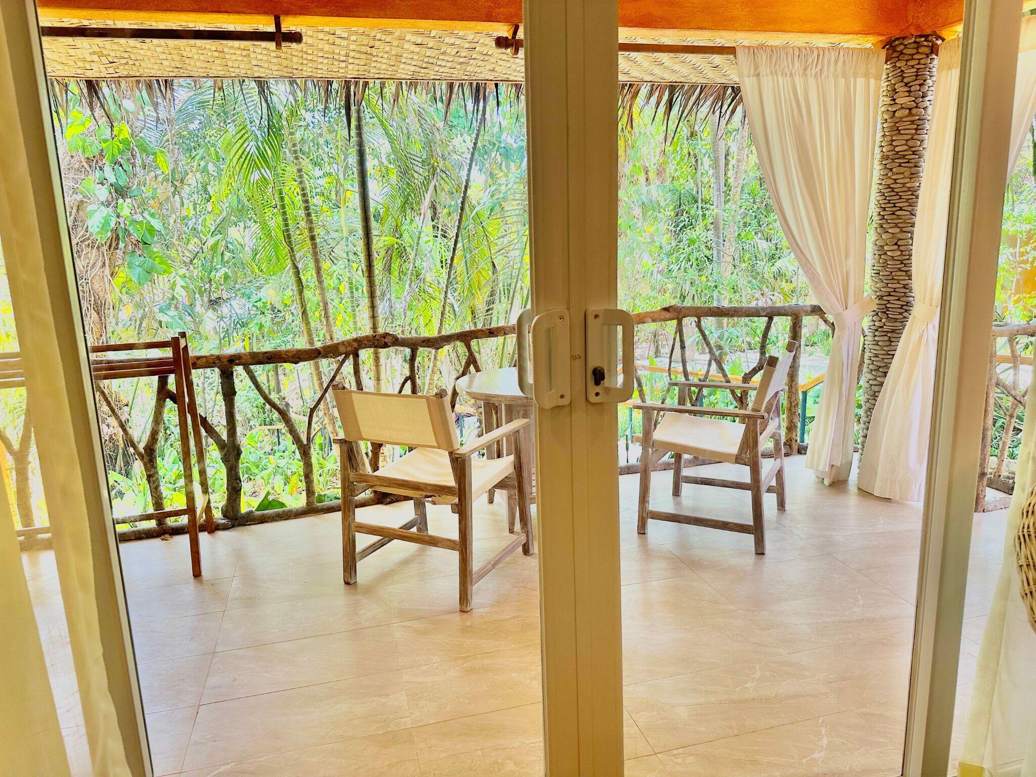 A wooden deck with two chairs and a table, surrounded by a bamboo fence and a view of dense greenery.