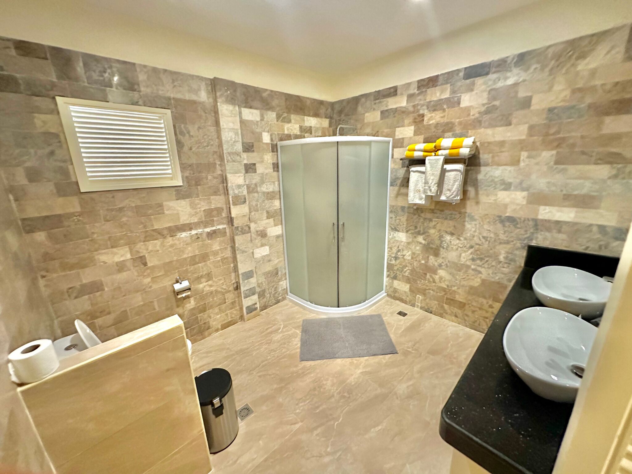 A bathroom with a glass shower enclosure, a toilet, a sink, and a towel rack with towels.
