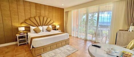 A hotel room with a large bed, a ceiling fan, a view of the outdoors, and a small table with items on it.