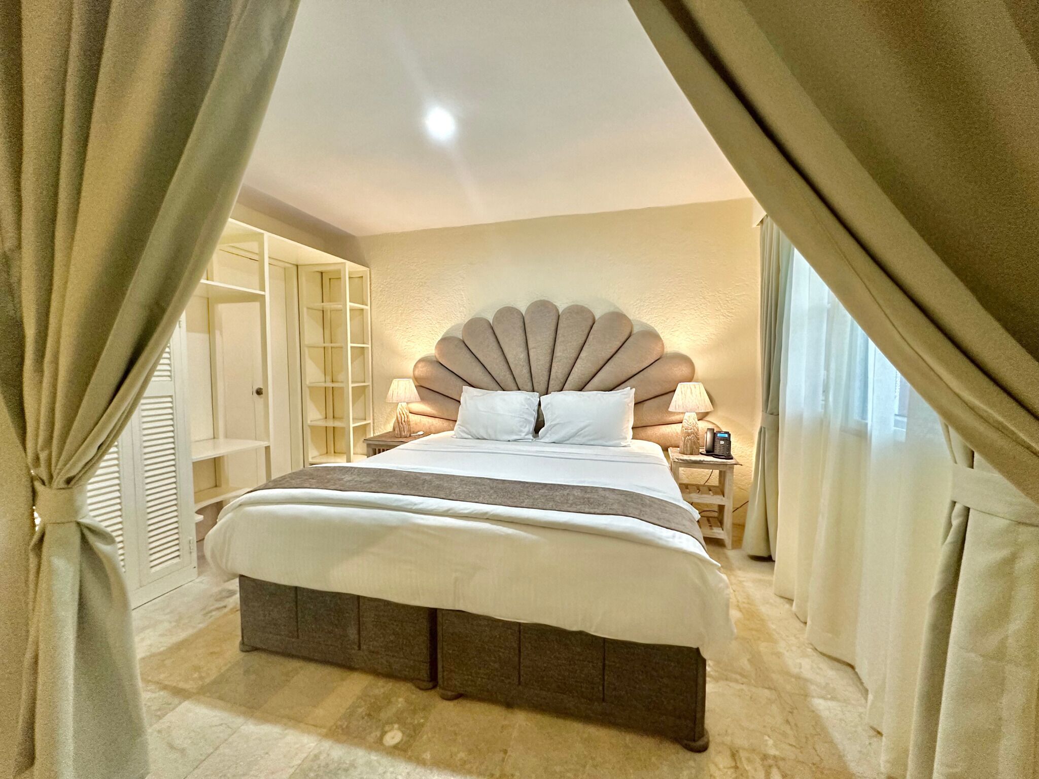 A spacious bedroom with a large bed, a built-in bench, a bedside table with a lamp, and a wardrobe with a mirror.