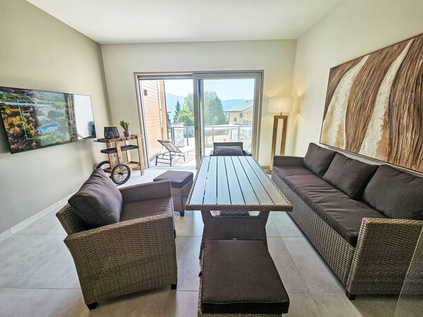 Una sala de estar moderna con muebles de mimbre, una mesa de madera y un ventanal con vistas al exterior.