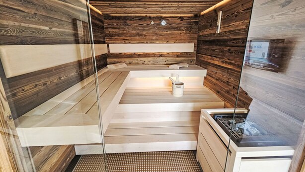 A sauna with wooden walls and a glass door, a bench, and a small table with a cup.
