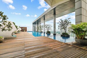 A rooftop infinity pool with a wooden deck, surrounded by modern architectural structures and potted plants. - Sorami by Kozystay - Senayan (Jakarta)