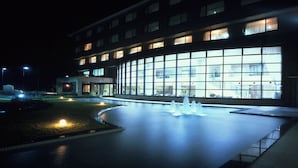 Un edificio con un'ampia facciata vetrata, una fontana nel cortile e un ingresso ben illuminato.